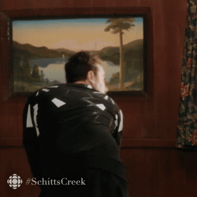 A Man Standing In Front Of A Painting That Says Schitts Creek On The Bottom GIF