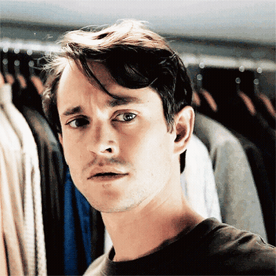 A Man Standing In Front Of A Rack Of Clothes Making A Face GIF