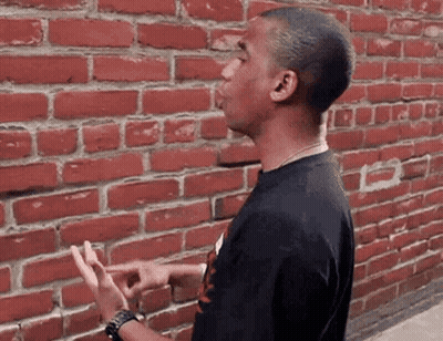 A Man Standing In Front Of A Red Brick Wall GIF