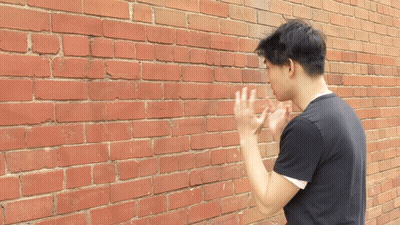 A Man Standing In Front Of A Red Brick Wall With His Hands Up GIF
