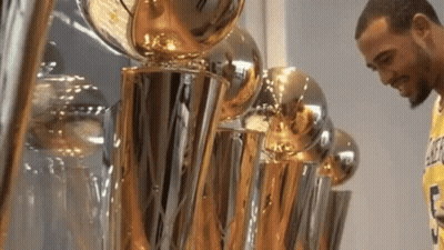 A Man Standing In Front Of A Row Of Trophies Including One That Says Lakers On It GIF