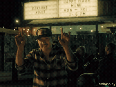 A Man Standing In Front Of A Sign That Says Happy Hour Menu GIF