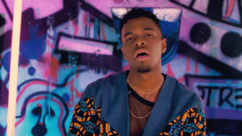 A Man Standing In Front Of A Wall With Graffiti On It That Says Tre GIF