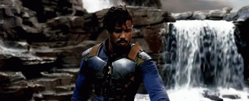 A Man Standing In Front Of A Waterfall Wearing A Blue Vest GIF