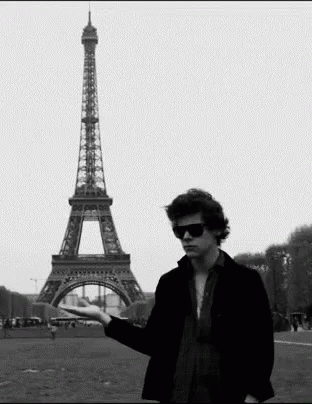 A Man Standing In Front Of The Eiffel Tower Holding Something In His Hand GIF
