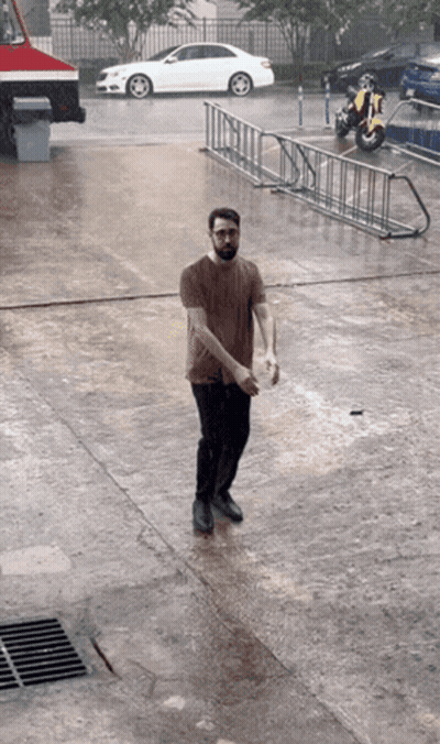A Man Standing In The Rain With A Motorcycle Parked Behind Him GIF