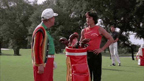 A Man Standing Next To A Red Golf Bag With The Word Converse On The Front GIF