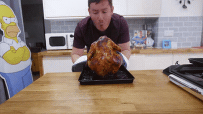 A Man Standing Next To A Roasted Chicken On A Table GIF