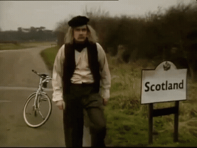 A Man Standing Next To A Sign That Says " Scotland " GIF