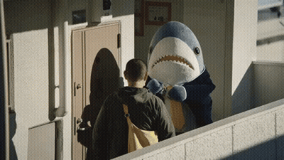 A Man Standing Next To A Stuffed Shark With A Backpack GIF