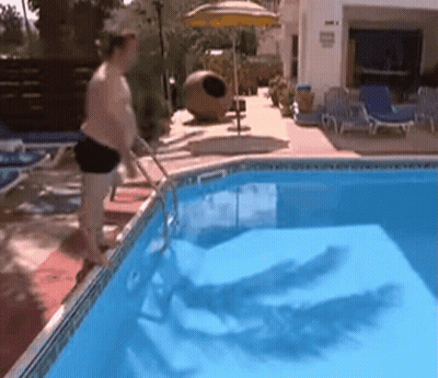 A Man Standing Next To A Swimming Pool With A Yellow Umbrella In The Background GIF