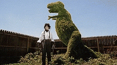 A Man Standing Next To A T-Rex Made Of Plants GIF