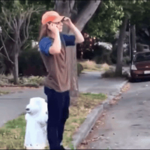 A Man Standing Next To A White Fire Hydrant Talking On His Cell Phone GIF
