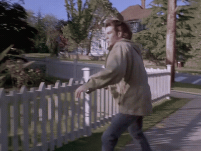 A Man Standing Next To A White Picket Fence Looking Over It GIF