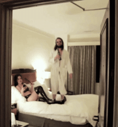 A Man Standing Next To A Woman On A Bed GIF