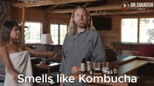 A Man Standing Next To A Woman Wrapped In A Towel With The Words " Smells Like Kombucha " Below Him GIF