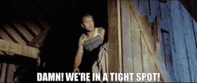 A Man Standing Next To A Wooden Wall With The Words Damn We 'Re In A Tight Spot . GIF