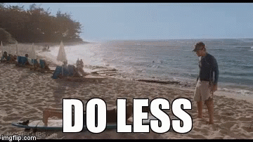 A Man Standing On A Beach Next To A Surfboard With The Words Do Less Written On It GIF