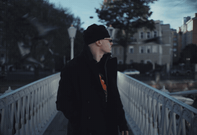 A Man Standing On A Bridge With A Building In The Background GIF