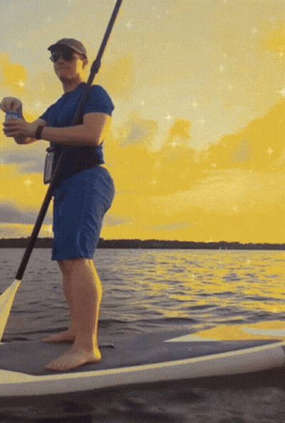 A Man Standing On A Paddle Board In The Water Holding A Can Of Bud Light GIF