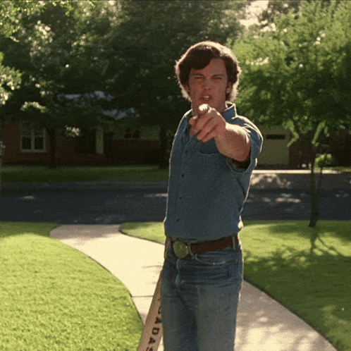A Man Standing On A Sidewalk Holding A Bat That Says Cadas On It GIF