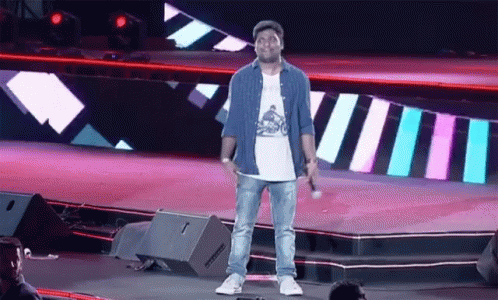 A Man Standing On A Stage With A Microphone In His Hand GIF