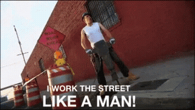 A Man Standing On A Street With A Sign That Says Road Work Ahead GIF