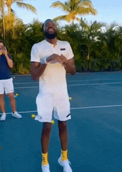A Man Standing On A Tennis Court With Tennis Balls Around His Legs GIF