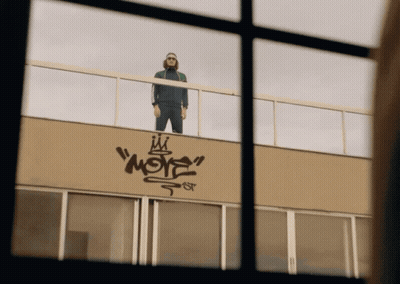 A Man Standing On Top Of A Building With Graffiti On The Side That Says " More " GIF