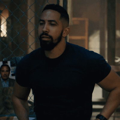 A Man Standing With His Arms Crossed In Front Of A Chain Link Fence GIF