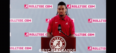 A Man Stands At A Podium In Front Of A Microphone Wearing A Red Shirt With The Letter A On It GIF