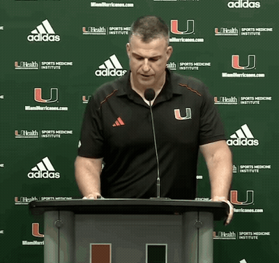 A Man Stands At A Podium In Front Of A Wall With Adidas Logos GIF