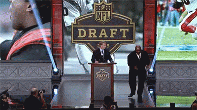A Man Stands At A Podium In Front Of An Nfl Draft Banner GIF