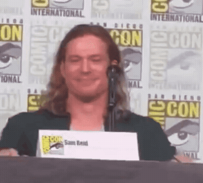 A Man Stands At A Podium With A Comic Con Sign In The Background GIF