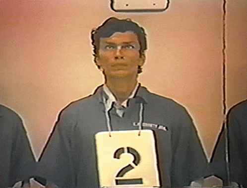 A Man Stands Behind A Sign That Says 2 GIF