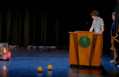 A Man Stands Behind A Wooden Podium With A Green Circle That Says ' Uc San Diego ' On It GIF