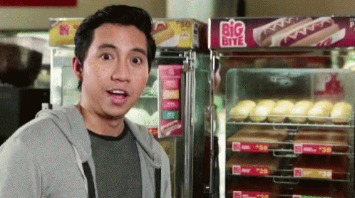 A Man Stands In Front Of A Big Bite Hot Dog Display GIF