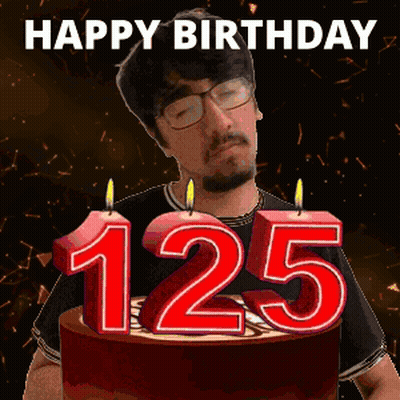 A Man Stands In Front Of A Birthday Cake With Candles That Say 125 GIF