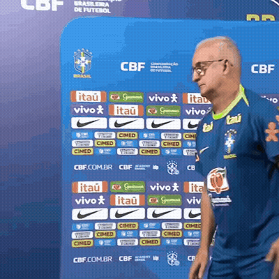 A Man Stands In Front Of A Blue Wall With Logos For Itau And Vivo GIF