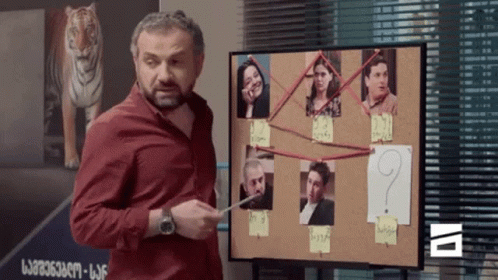 A Man Stands In Front Of A Bulletin Board With A Question Mark In The Middle GIF