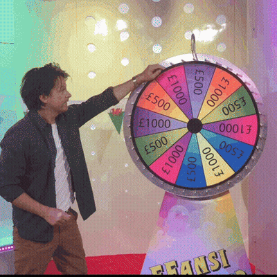 A Man Stands In Front Of A Colorful Spinning Wheel That Says ' Fransi ' On It GIF