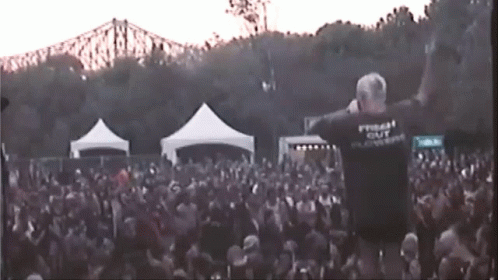 A Man Stands In Front Of A Crowd Wearing A T-Shirt That Says Freak Out GIF