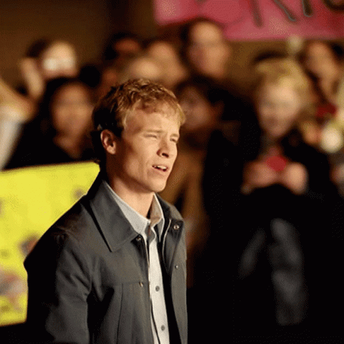 A Man Stands In Front Of A Crowd With A Sign That Says " I Love You " In The Background GIF