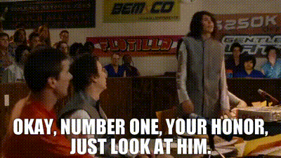 A Man Stands In Front Of A Crowd With A Sign That Says " Okay Number One Your Honor Just Look At Him " GIF