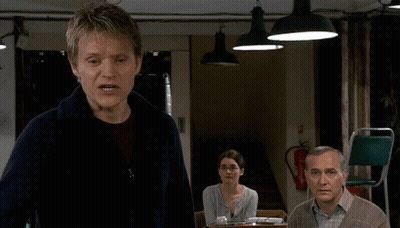 A Man Stands In Front Of A Fire Extinguisher And A Woman Sitting At A Table GIF