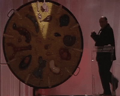 A Man Stands In Front Of A Large Circular Display Of Food Items GIF