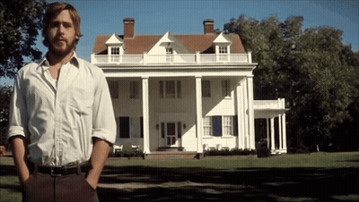 a man stands in front of a large white house with his hands in his pockets