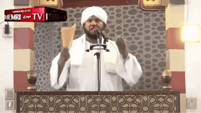 A Man Stands In Front Of A Microphone And A Sign That Says Memri Tv On It GIF