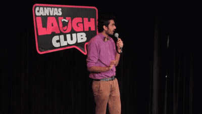 A Man Stands In Front Of A Microphone In Front Of A Sign That Says Canvas Laugh Club GIF