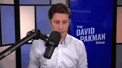 A Man Stands In Front Of A Microphone In Front Of A Sign That Says " The David Pakman Show " GIF